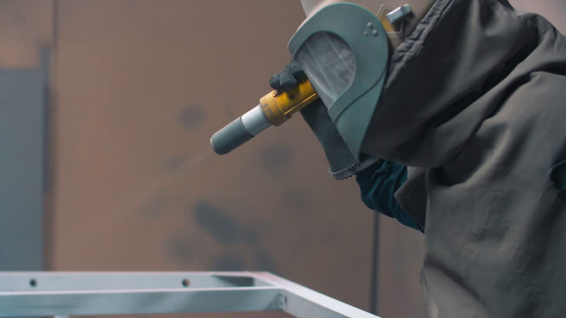 A worker welding in a factory, wearing a protective mask and gloves, working on a metal frame.