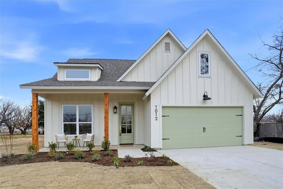 A modern two-story house with a white exterior, a green garage door, and a front porch with two chairs and plants. The house number 1012 is visible next to the front door. Northlake, TX is growing and is now served by Ready Surface dustless blasting.