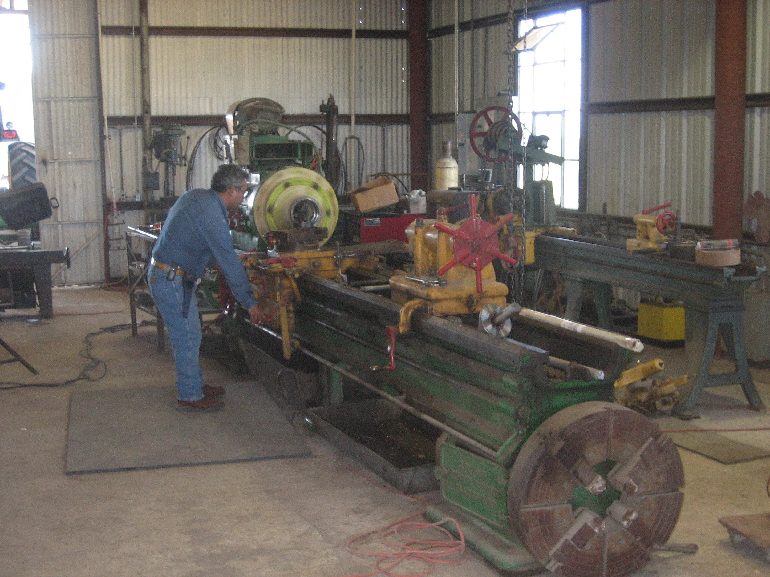 A man working with industrial machinery in a workshop or factory, surrounded by metal tools and equipment.