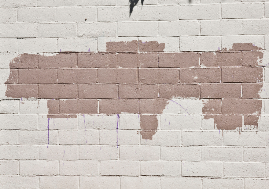 A painted brick wall with an outline of the state of Texas, partially painted in brown.