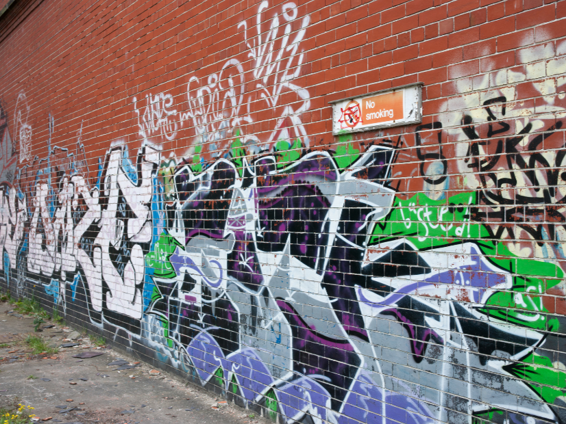 Graffiti covering a red brick wall with a 'No Smoking' sign, which is no match for dustless blasting as removal would increase property values.