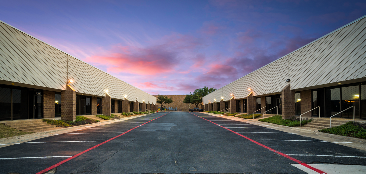 Empty parking lot with two rows of commercial buildings and a colorful sunset sky