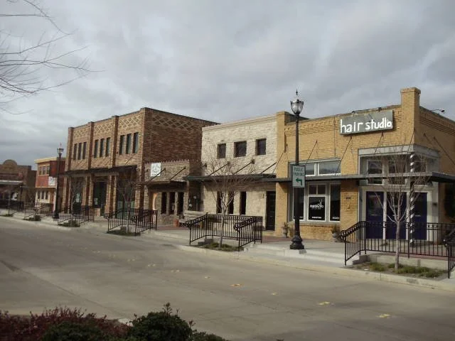 A small downtown street in Roanoke, TX with several businesses including a hair studio, under an overcast sky. Protecting historical building and removing graffiti by Ready Surface