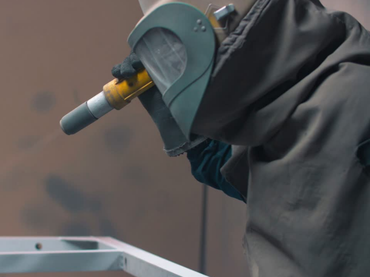 A person welding metal with a welding helmet and gloves in a workshop.
