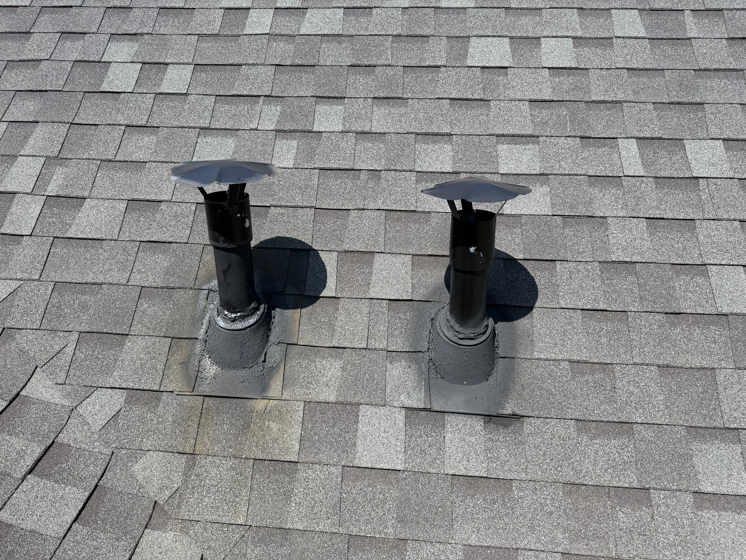 Two black roof vents on a gray shingled roof.