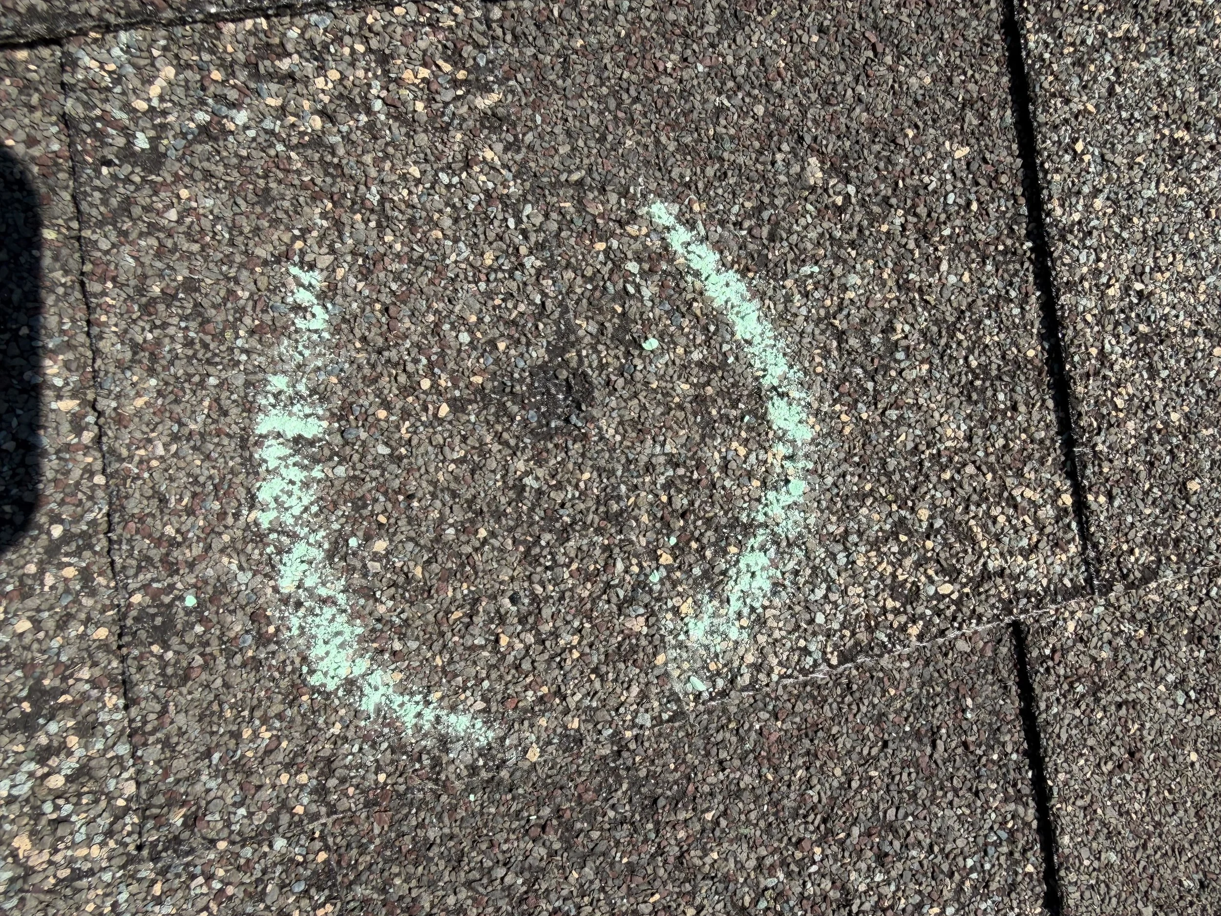 Close-up of a gravel surface with white chalk circling hail impact.