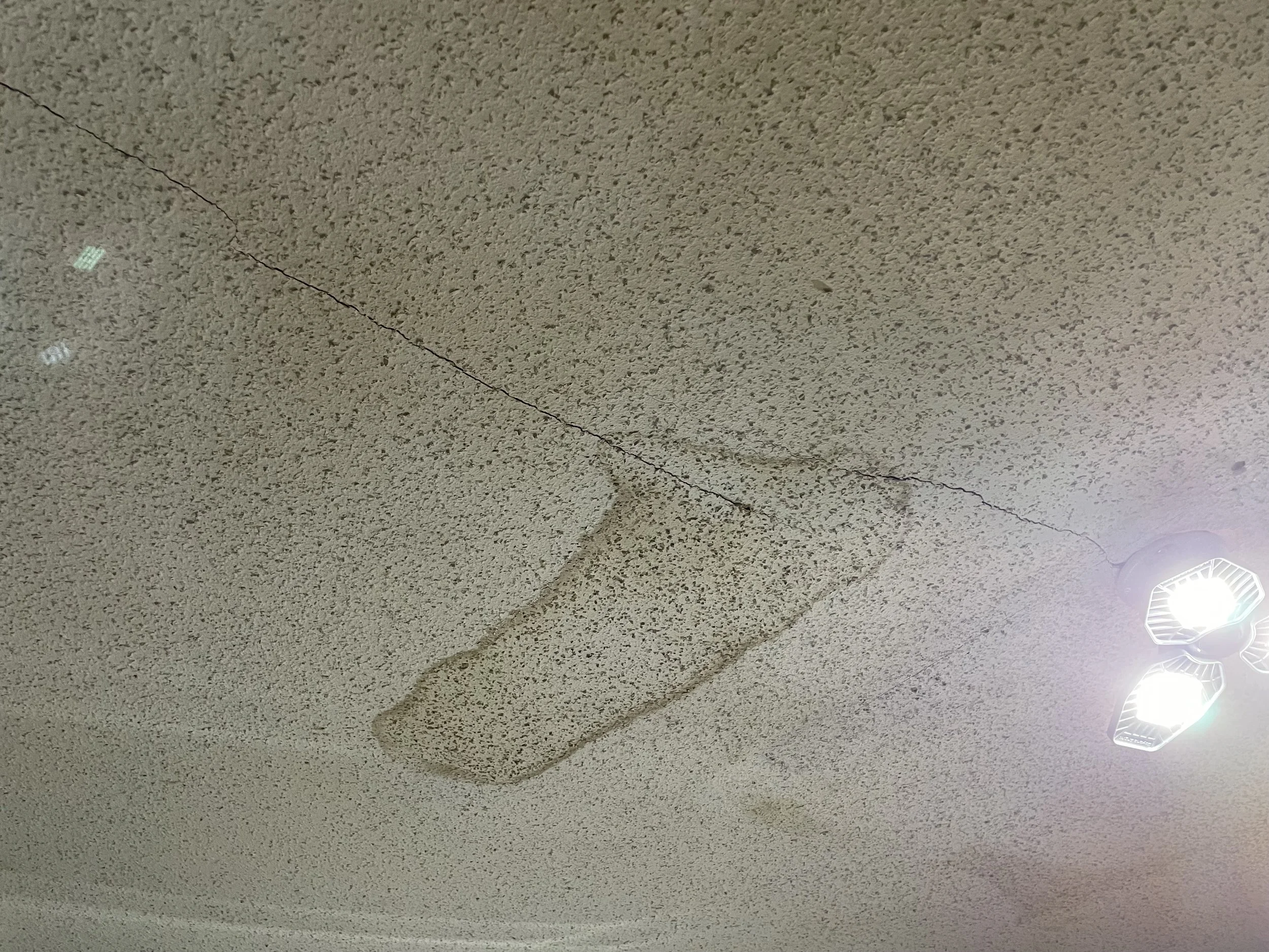 Ceiling with textured surface, visible cracks, and water stains from roofing leak.