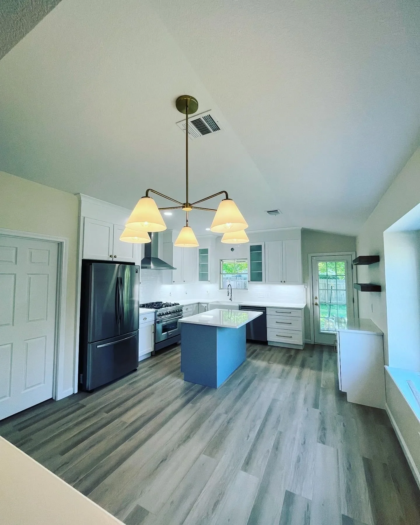 Modern kitchen with white cabinets, gray island, stainless steel appliances, hardwood flooring, and a unique chandelier with six lamps.
