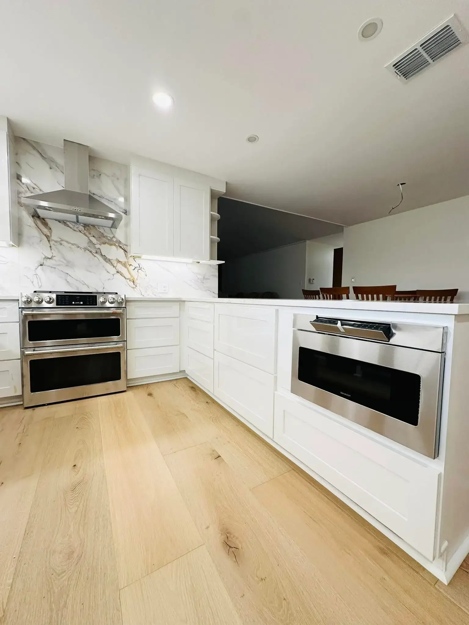 Modern kitchen with white cabinets, stainless steel appliances, marble backsplash, and light wooden flooring.
