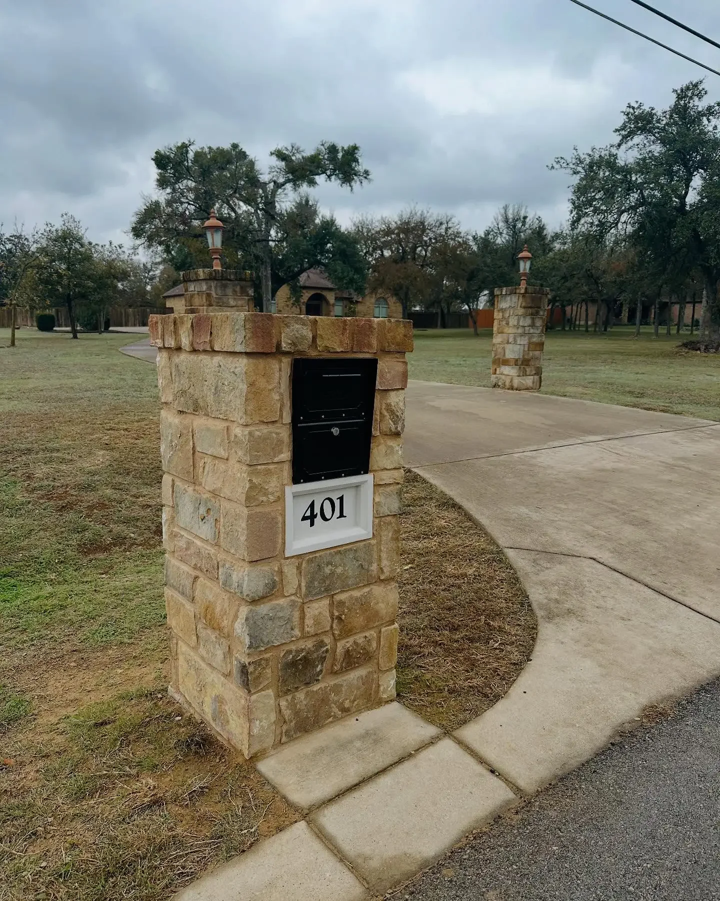 A stone mailbox with house number 401, located at the corner of a driveway in a residential neighborhood with trees and cloudy sky.