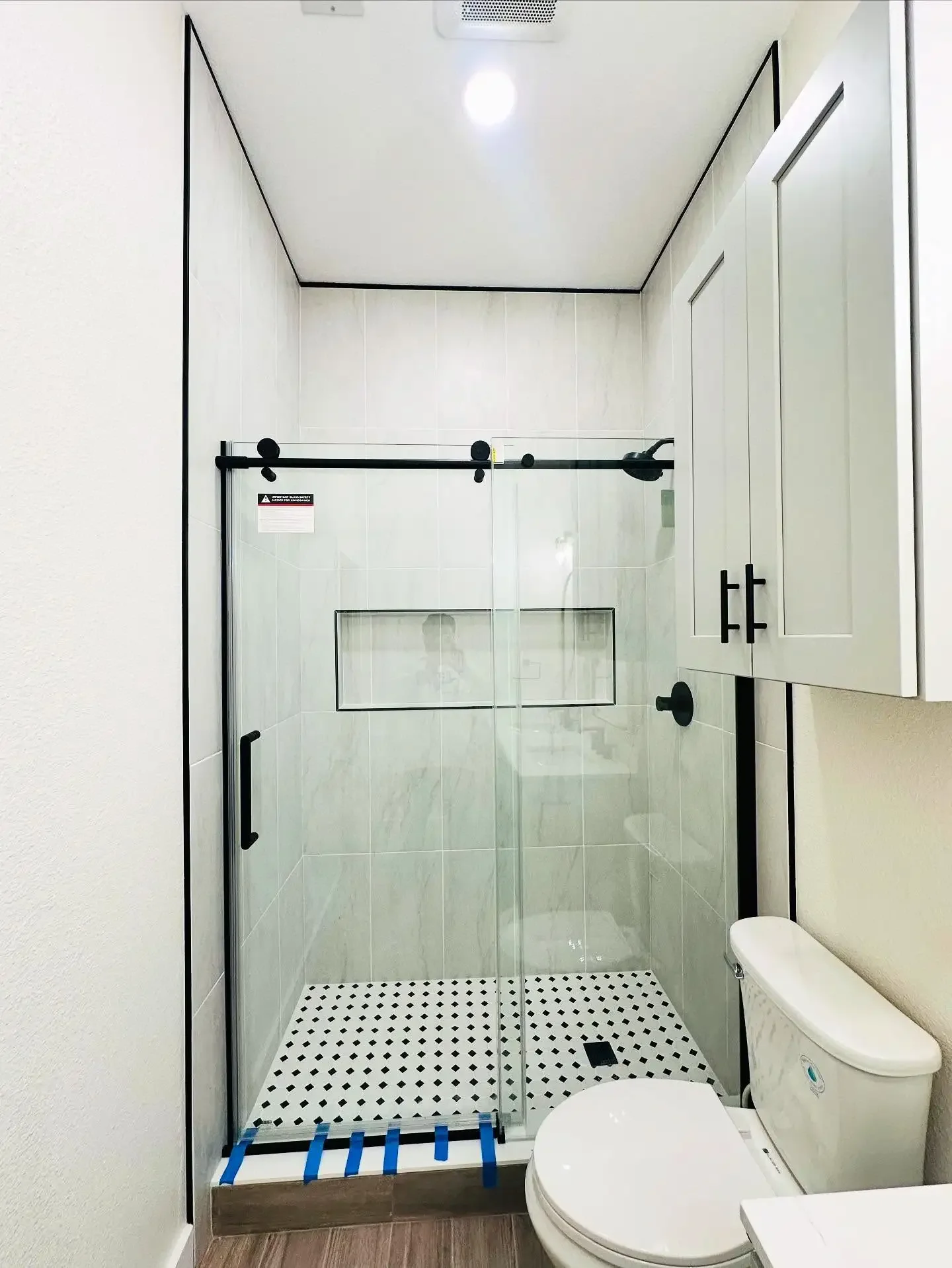 Bathroom with a glass shower enclosure, black fixtures, white cabinetry, a toilet, and wood-look flooring.