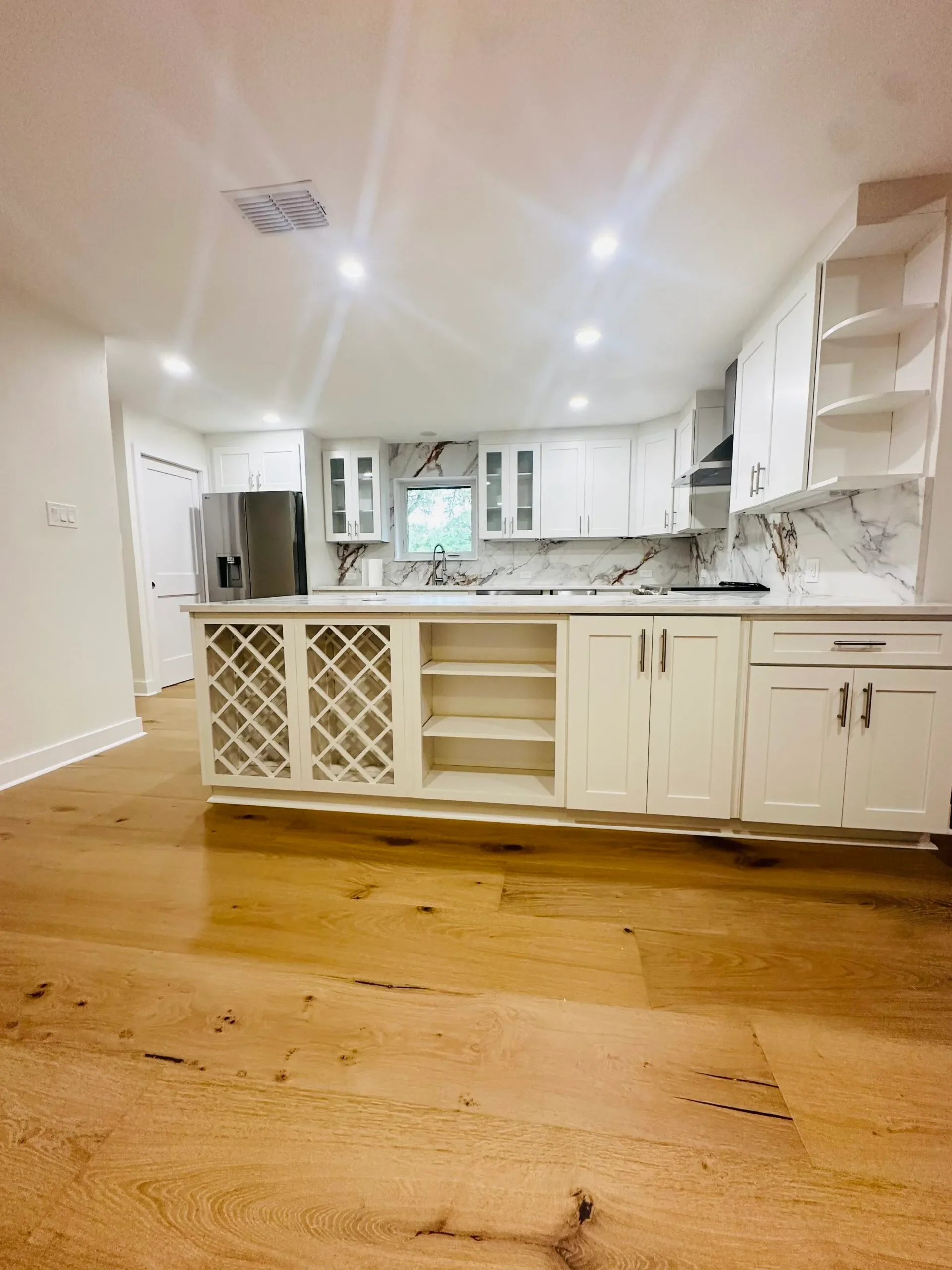 Modern kitchen with white cabinets, marble backsplash, stainless steel refrigerator, and a wooden floor.
