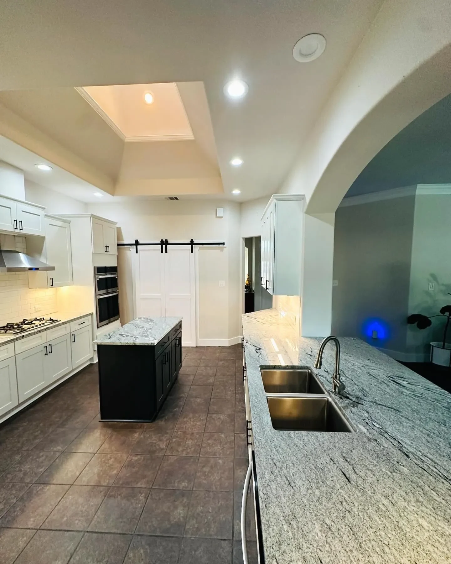 Modern kitchen with white cabinets, black island, granite countertops, and tiled floor.