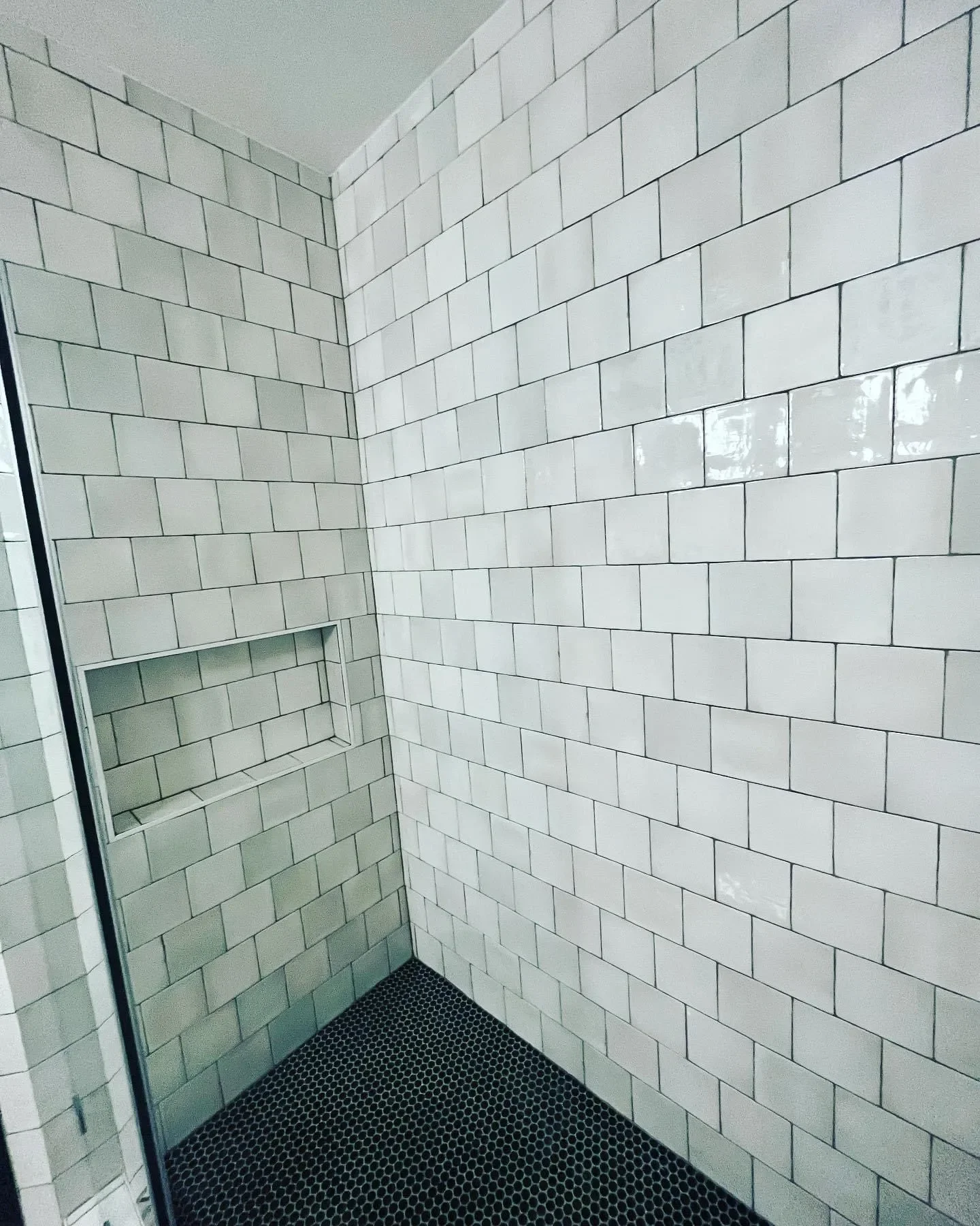 A clean, modern shower with white subway tile walls, a built-in rectangular shower niche, and black hexagonal floor tiles.