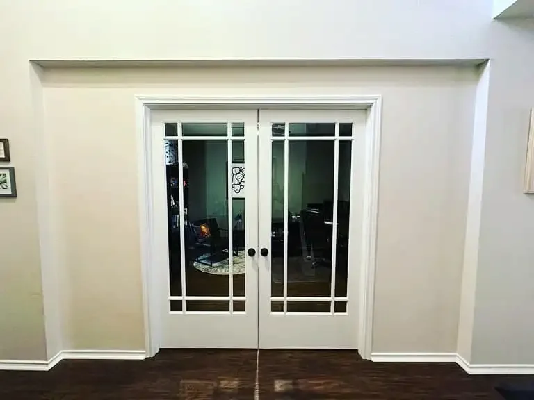 Sliding glass door with white framing and decorative grid pattern, leading to a living room with dark furniture.