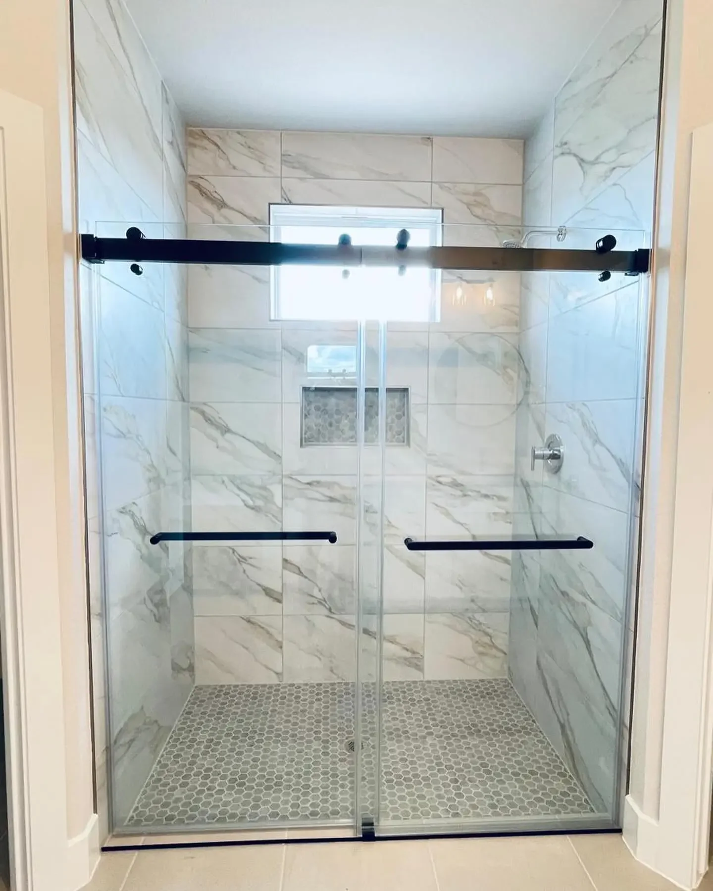 Bathroom shower with glass doors, marble tiles on the walls, a small window, a niche with a decorative backsplash, and a ceiling light.