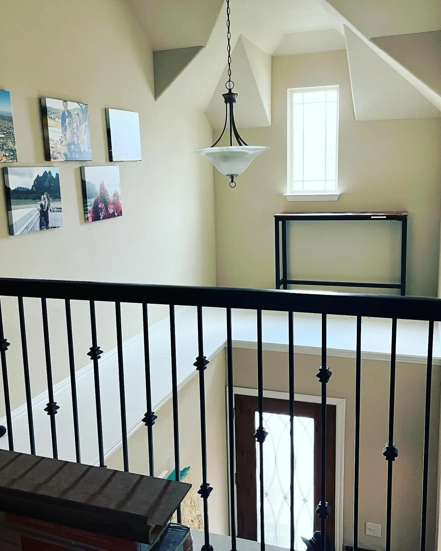 Interior view of a house entryway with a staircase, black railing, a hanging light fixture, a window, and framed photos on the wall.