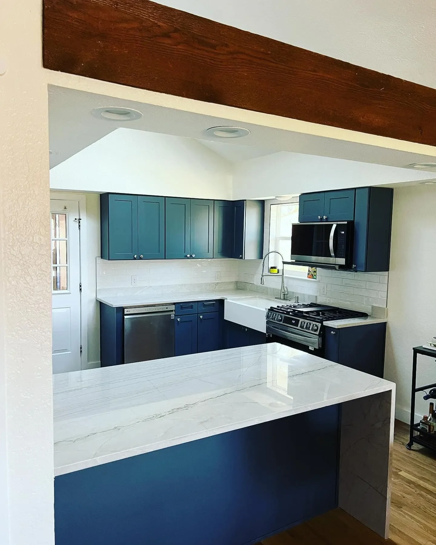 Modern kitchen with blue cabinets, white marble countertops, stainless steel appliances, and a white backsplash with subway tiles.