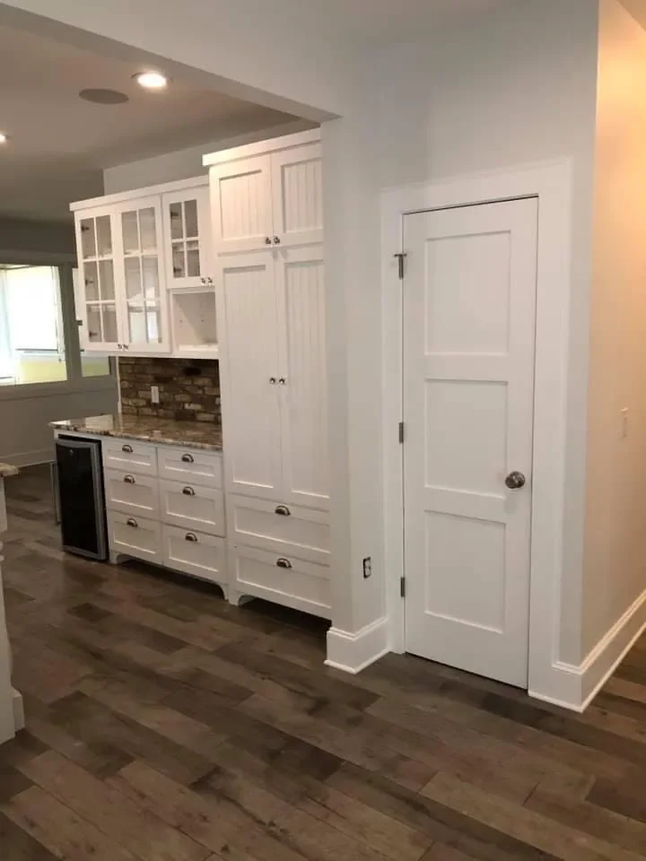 White kitchen cabinets with glass-paneled doors, a wooden countertop, and a brick backsplash, in a modern home interior.