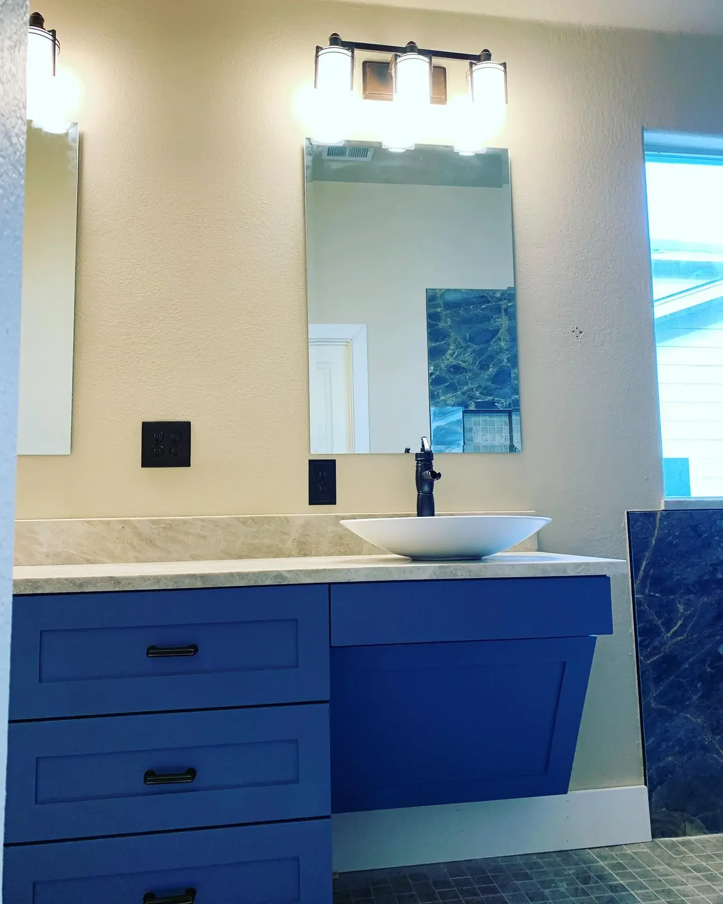 Bathroom vanity with blue cabinet, white countertop, vessel sink, black faucet, mirror, and wall-mounted light fixture.