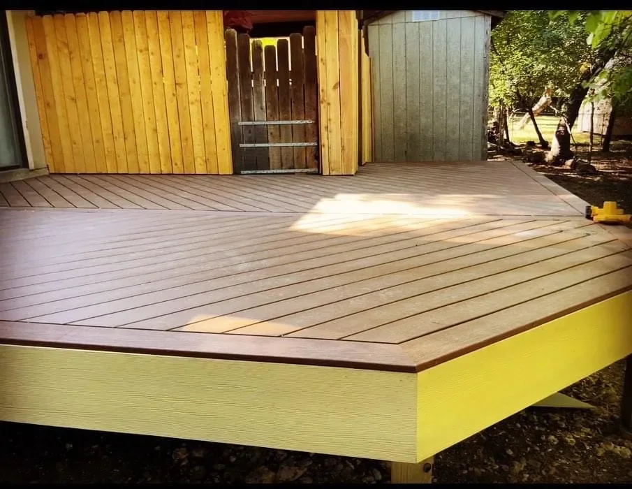 A newly built wooden deck outdoors with a natural wood finish and a yellow-painted side.