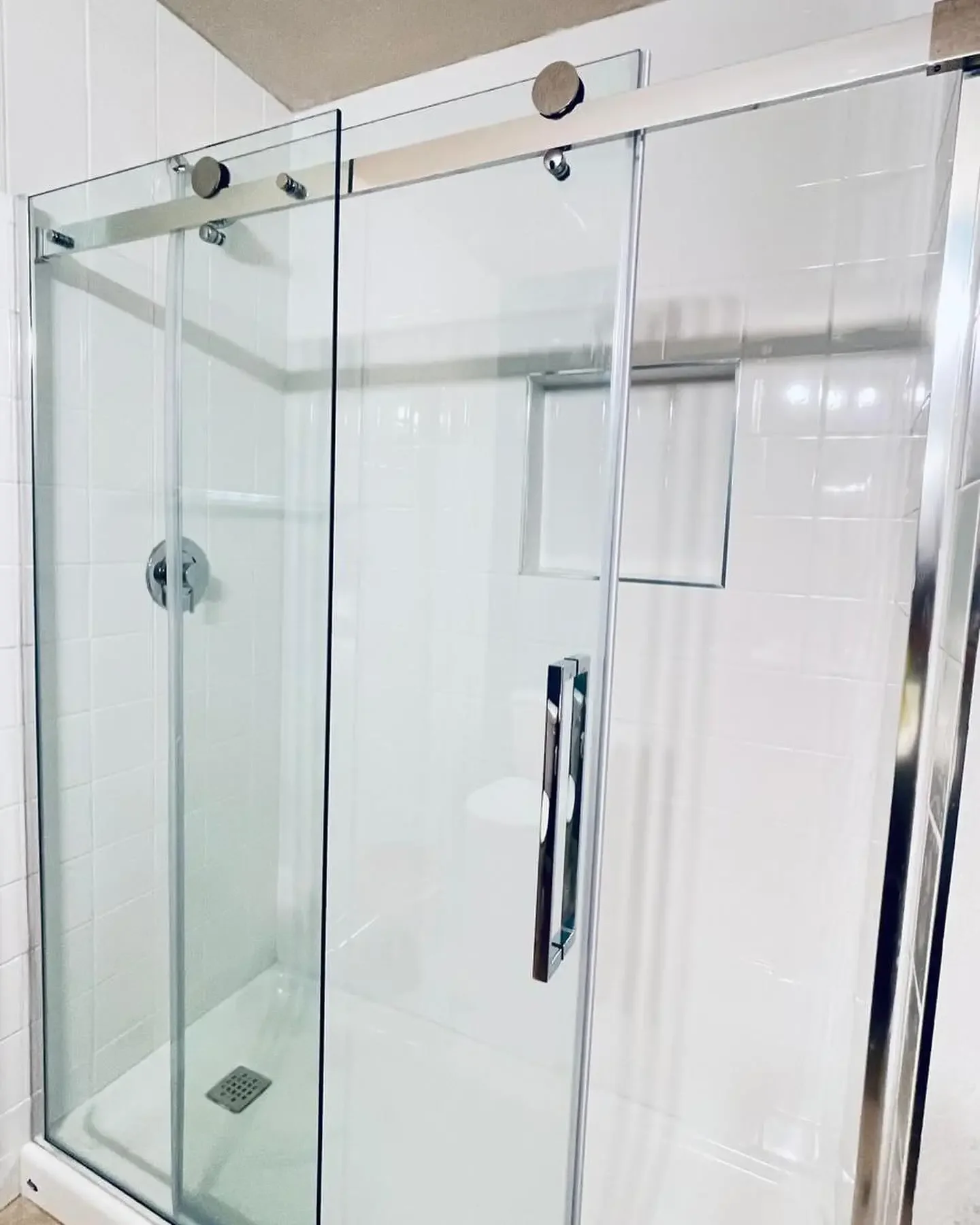 A modern glass shower enclosure with clear glass panels, a metal handle, and a tiled shower wall with a small built-in niche for toiletries.