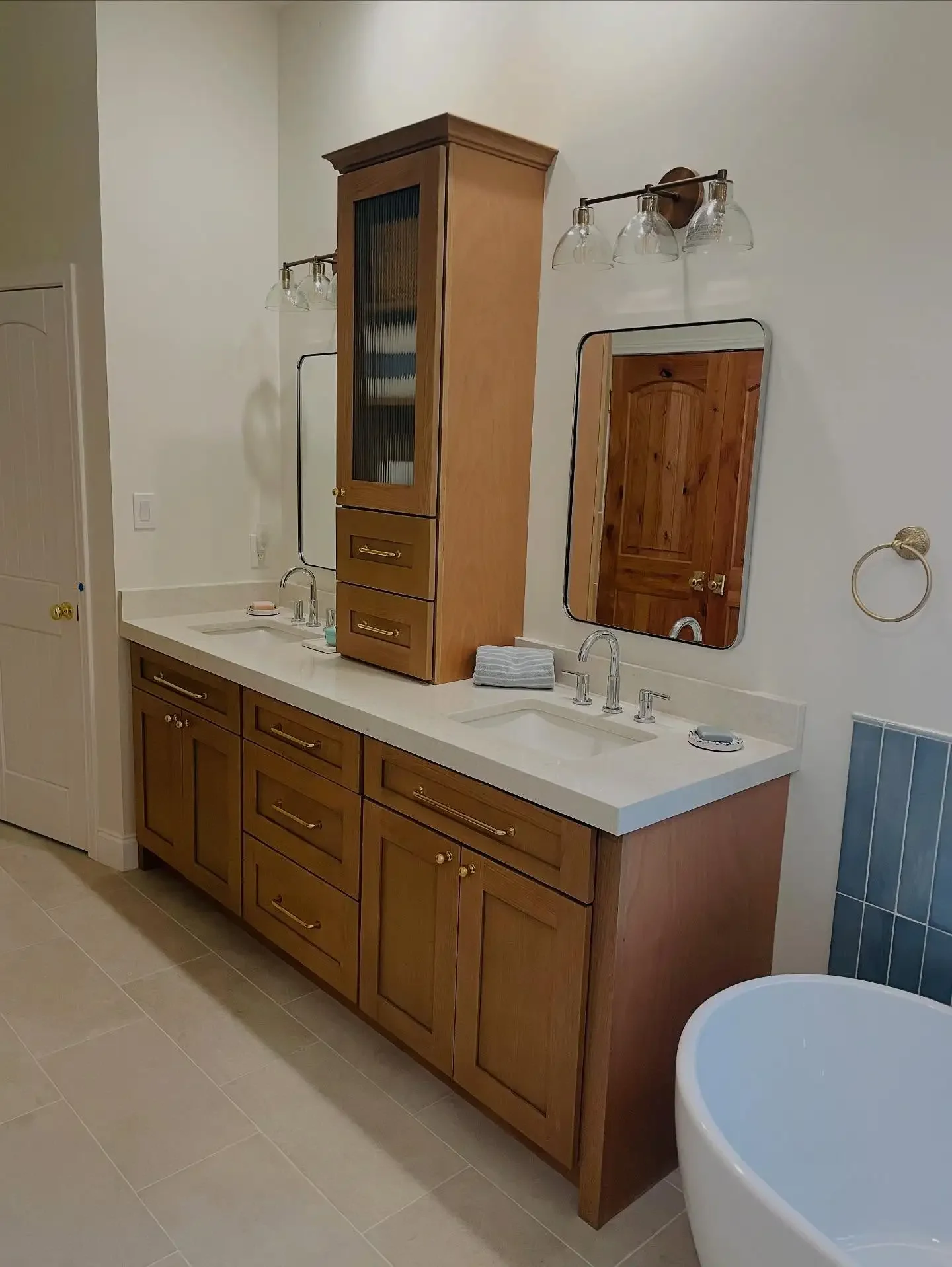Bathroom vanity with a double sink, wooden cabinets, a tall wooden medicine cabinet, and two mirrors, with a white bath tub in the foreground.
