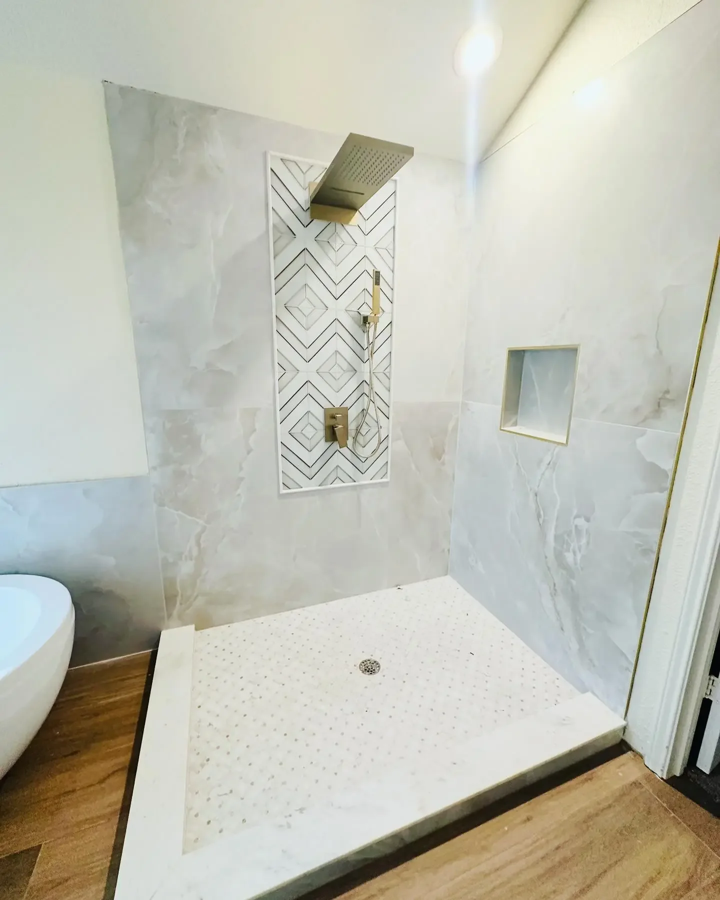 Modern bathroom shower area with a rainfall showerhead, a handheld showerhead, a built-in shower niche, and marble tiles.