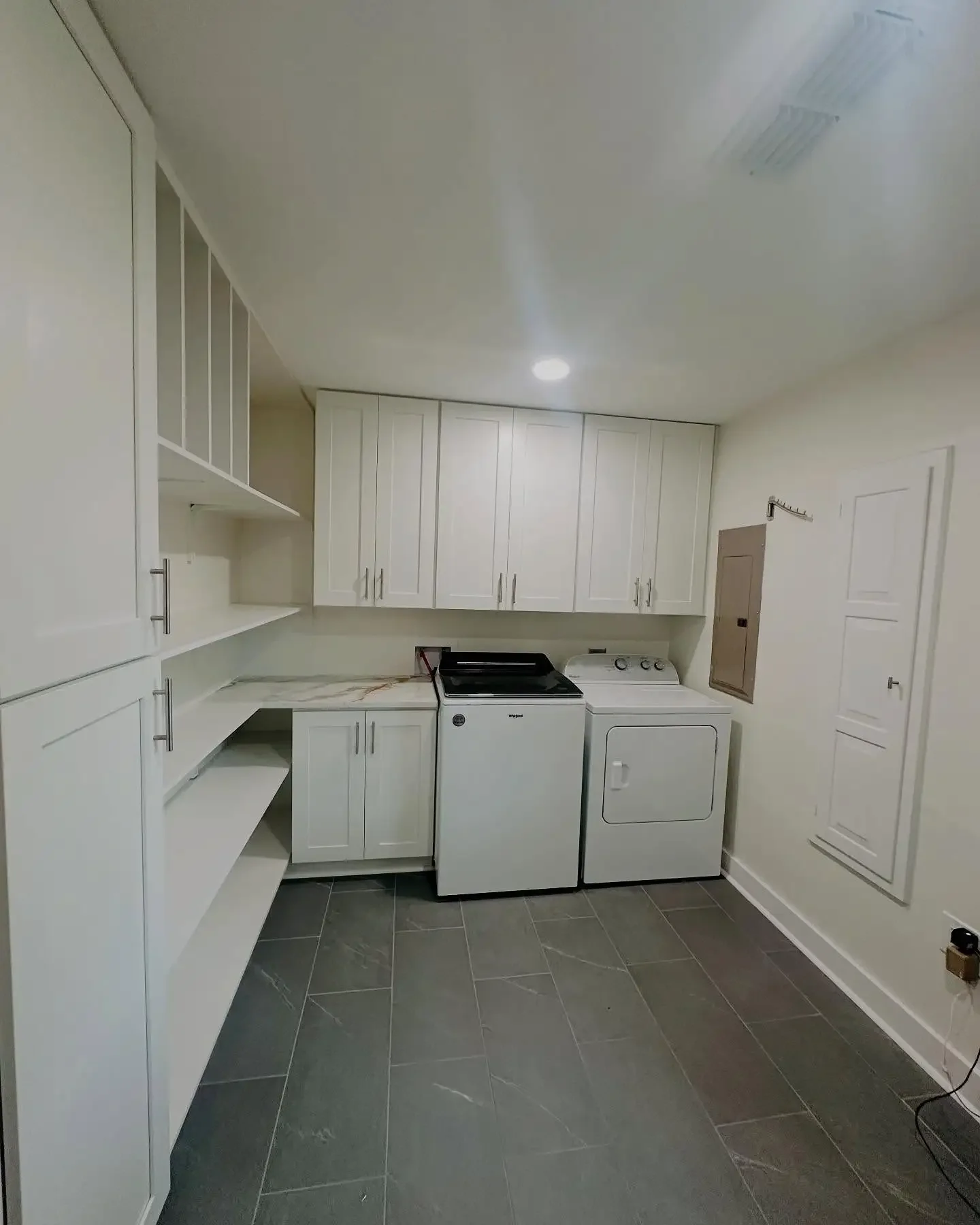 Laundry room with white cabinets, a washing machine, a dryer, and a gray tiled floor.