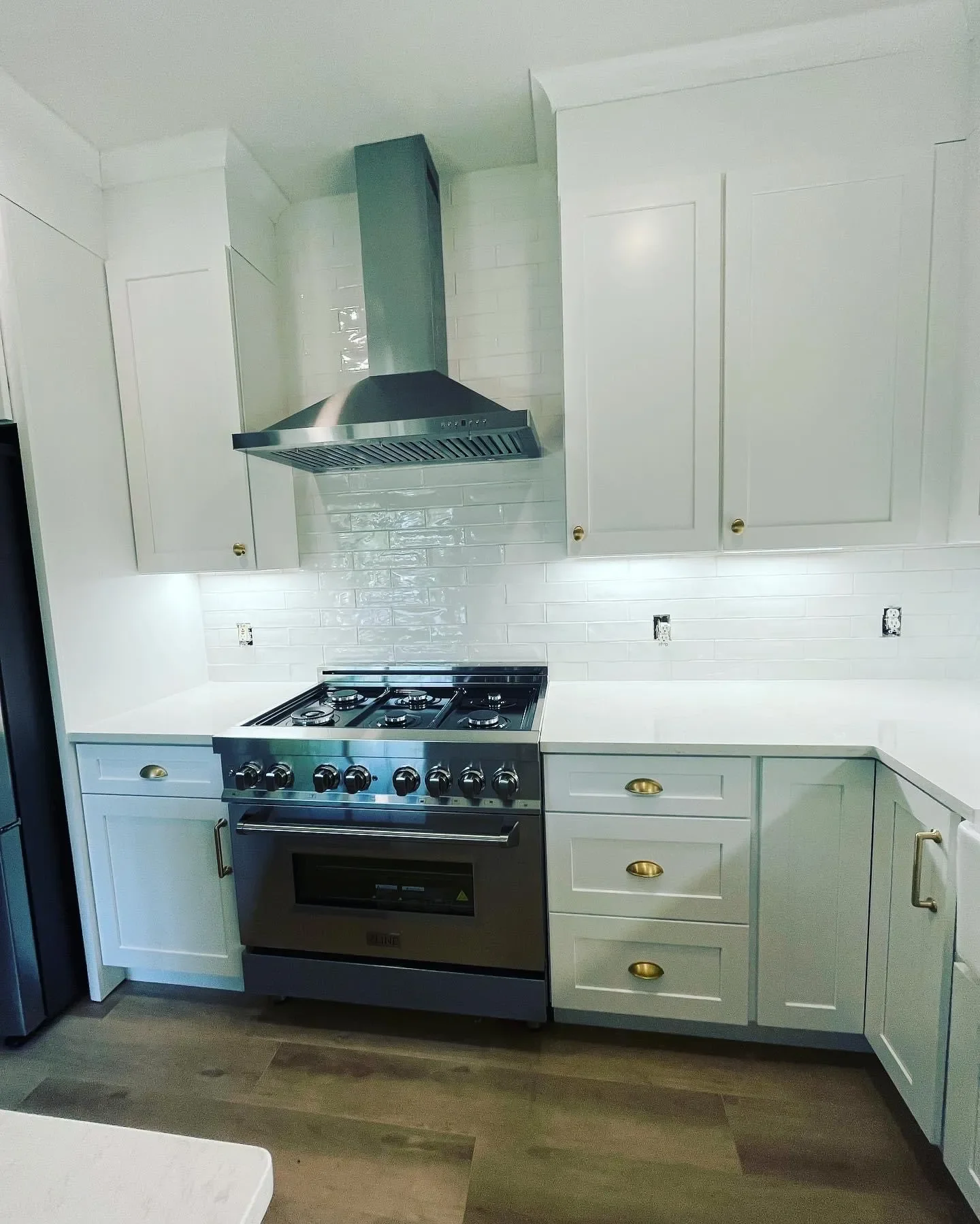 Modern kitchen with white cabinets, gold handles, stainless steel stove with oven, and stainless steel range hood.