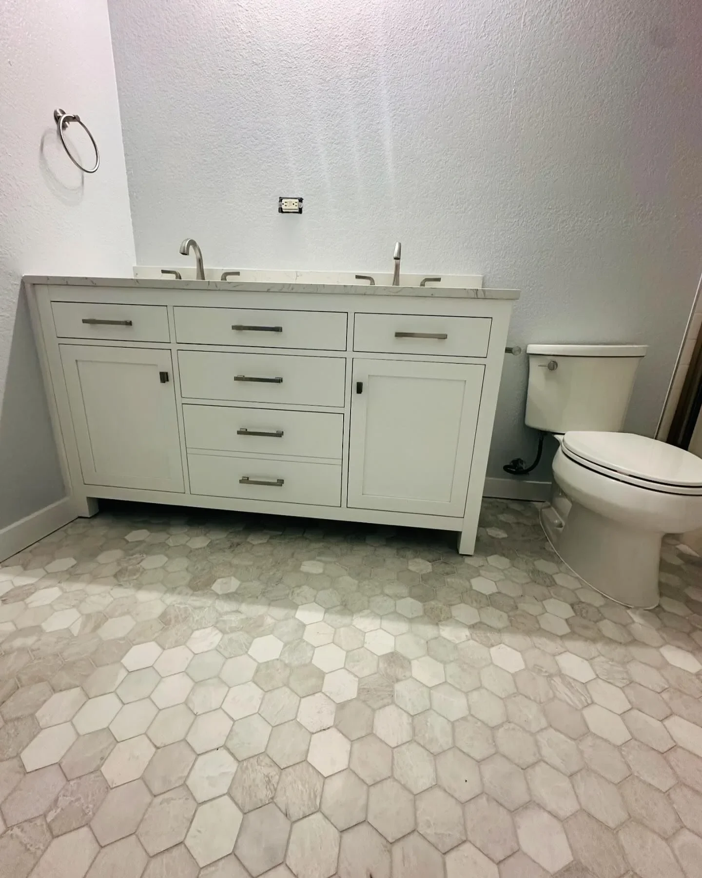 Bathroom with white vanity, dual sinks, and toilet, hardwood floor with hexagonal tiles.