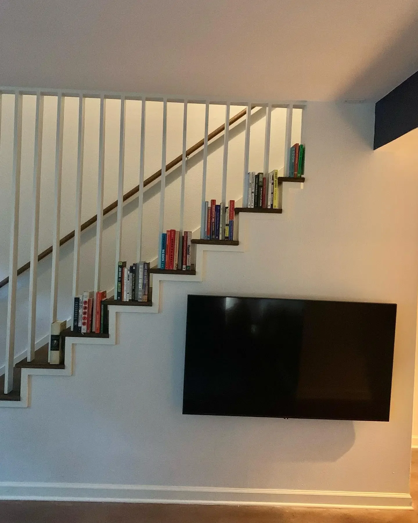Staircase with books placed along the steps and a mounted flat-screen TV on the wall underneath.