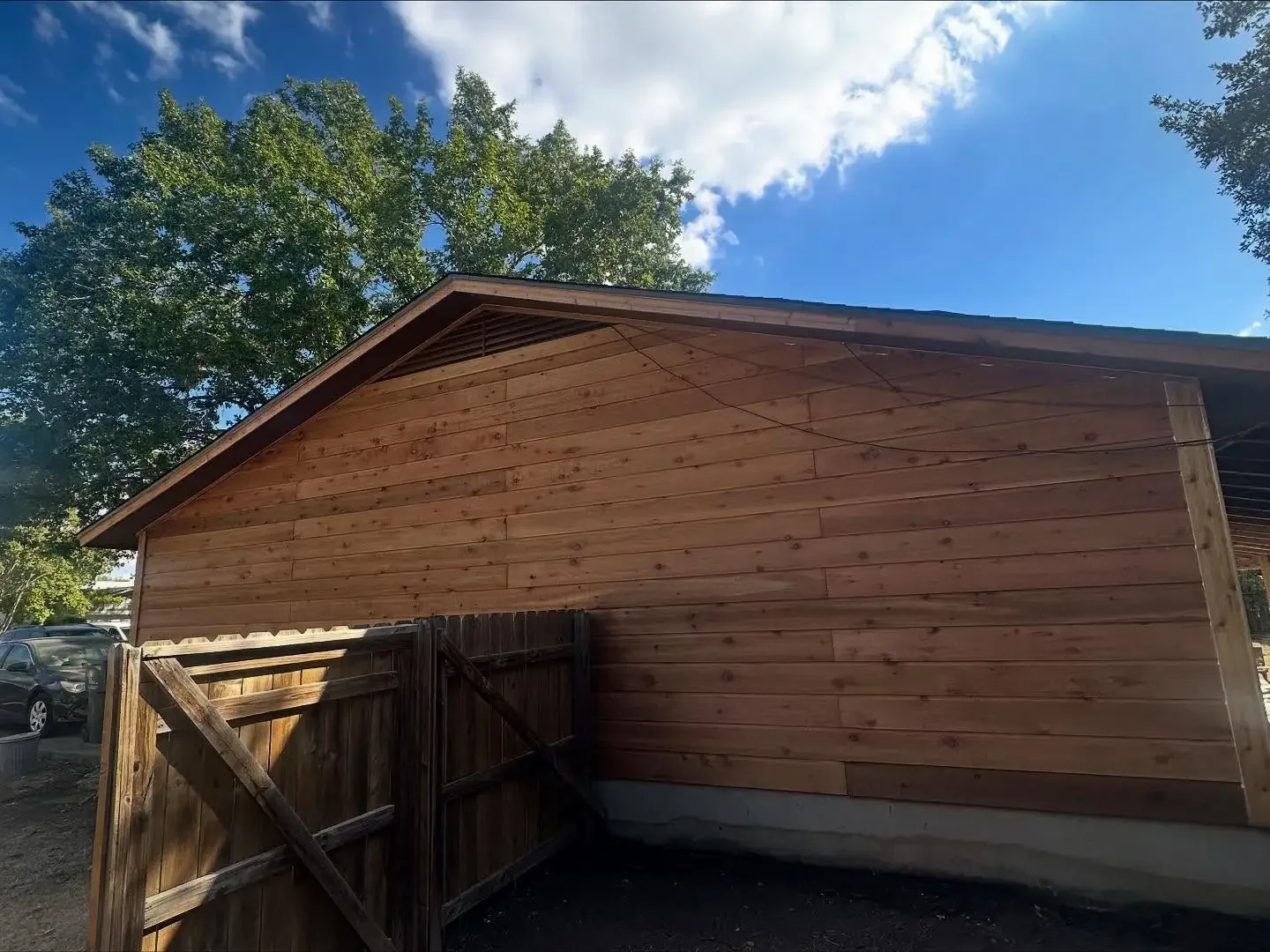 Side view of a wooden building with a sloped roof, surrounded by trees and a clear blue sky.