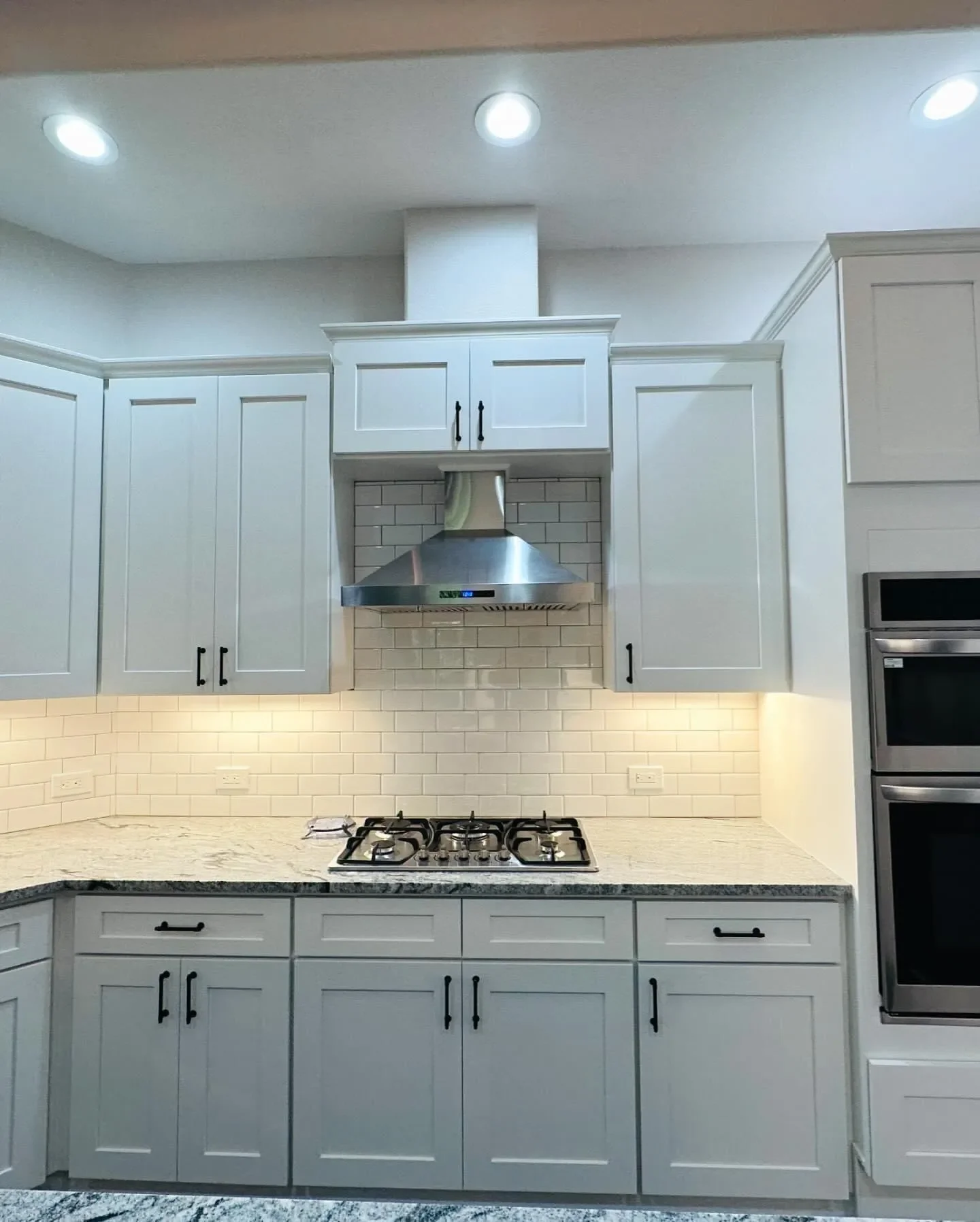 Modern kitchen with white cabinets, a stainless steel range hood, a gas stove, a granite countertop, and white subway tile backsplash.