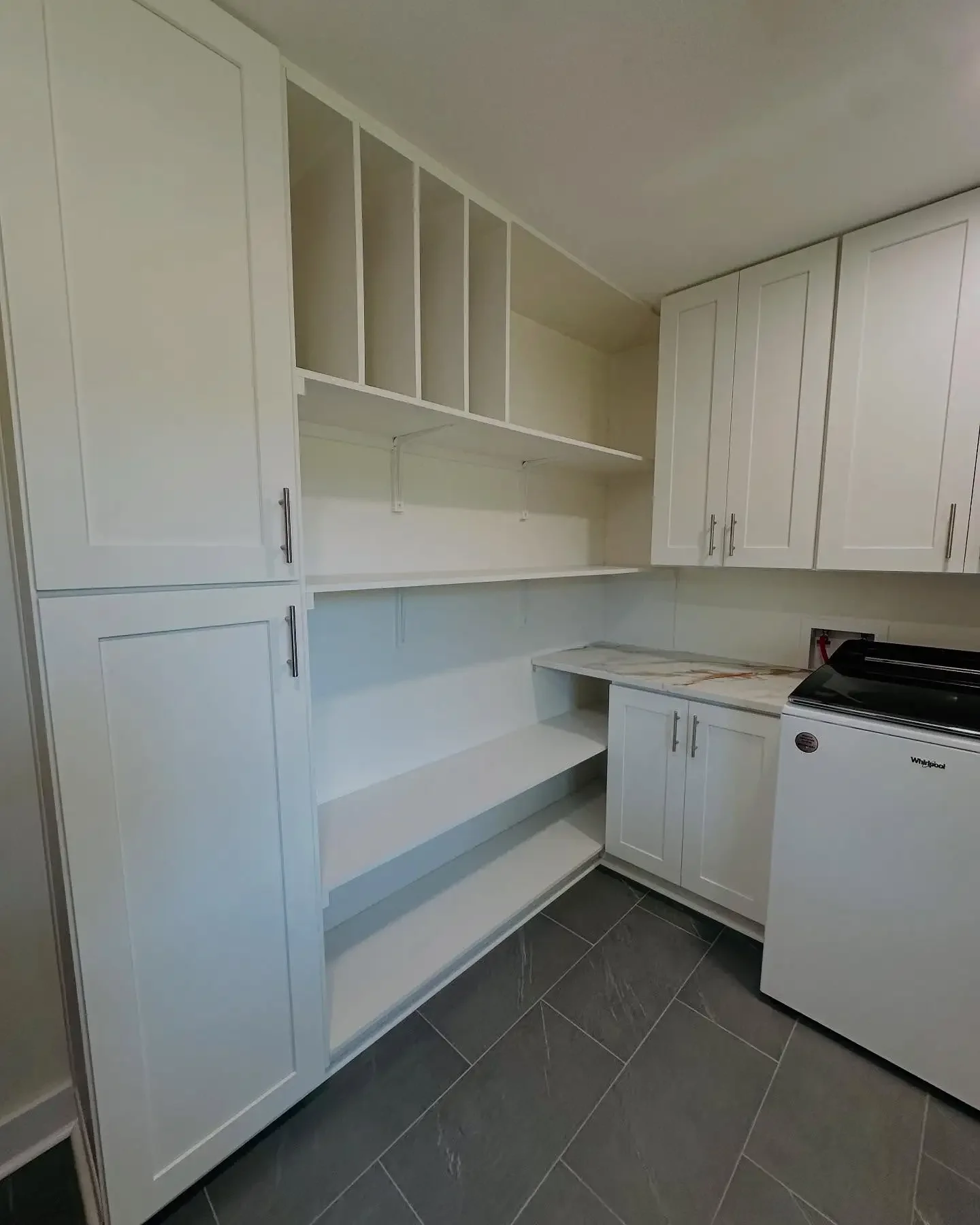 Laundry room with white cabinets and open shelving, a marble countertop, and a white washing machine on the right.