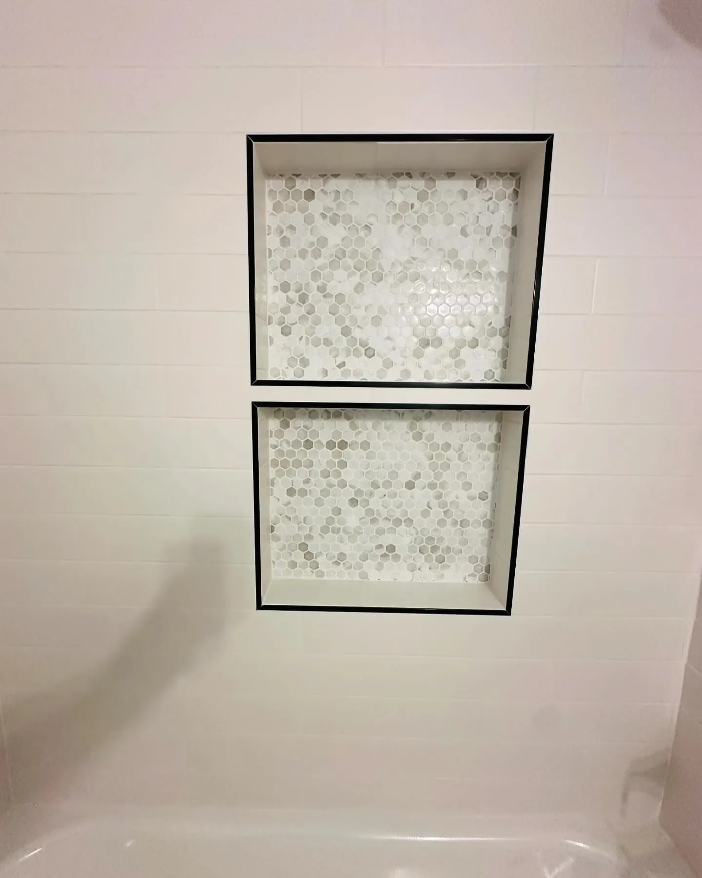 Two shower niches with hexagonal tile backsplashes built into a white tiled shower wall.