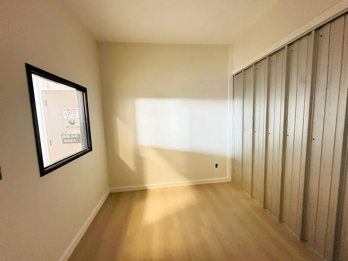 Empty room with a window on the left wall, a beige wall with sunlight, and a large metal closet on the right side.