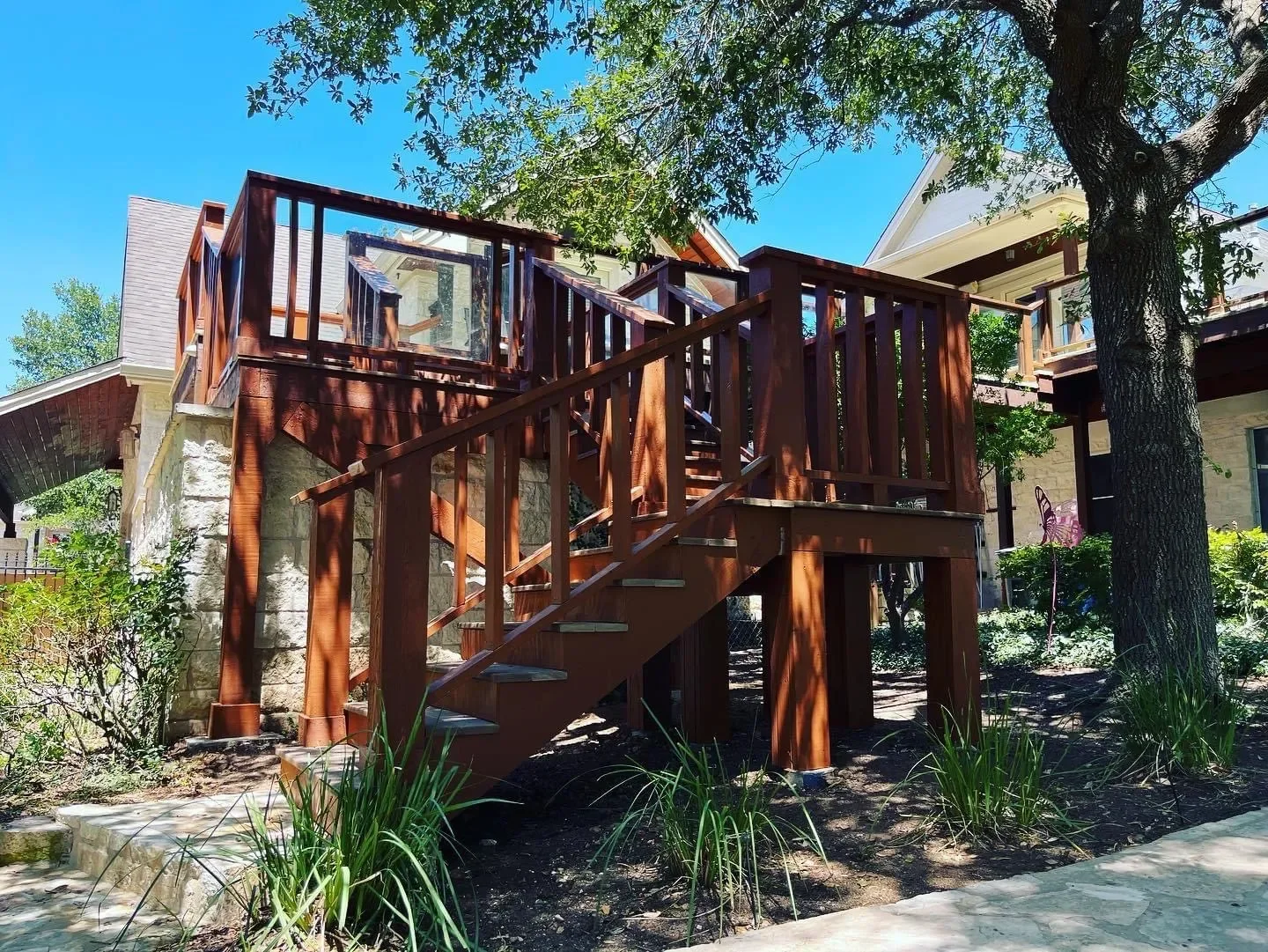 Backyard with wooden deck stairs, surrounded by greenery and trees, on a sunny day.