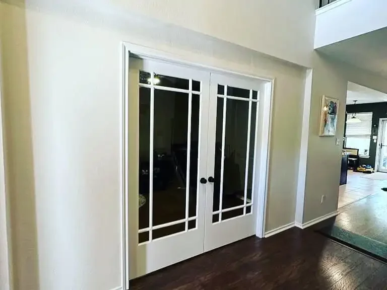 White double doors with glass panels inside a house, leading to another room