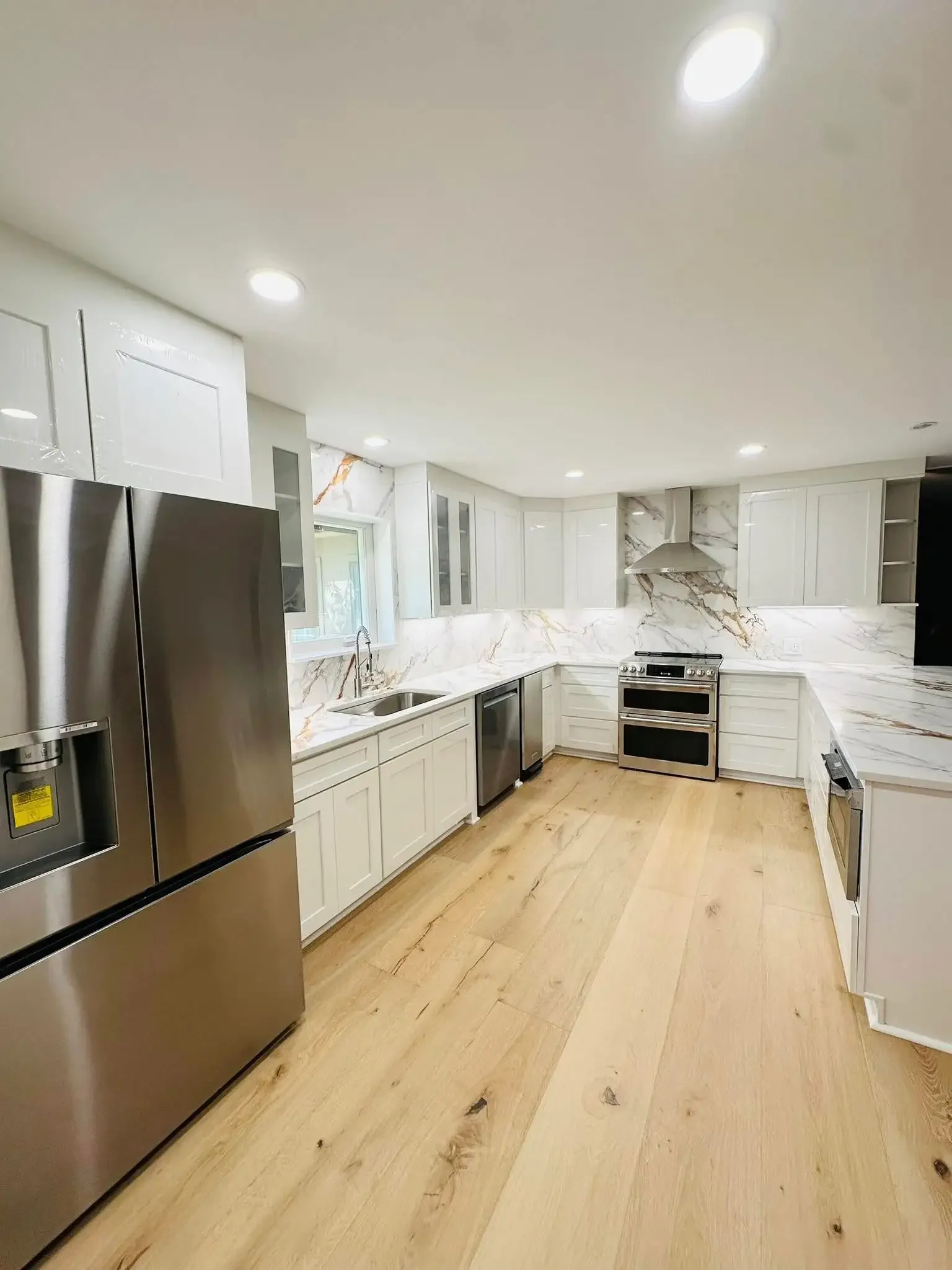 Modern kitchen with white cabinets, marble countertops, stainless steel appliances, and light wood flooring.