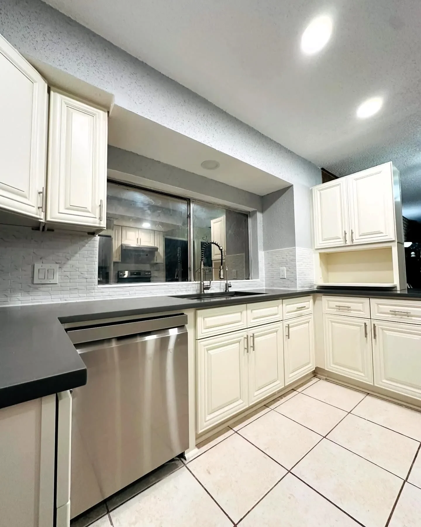 Kitchen with white cabinetry, black countertop, stainless steel dishwasher, and a window above the sink.