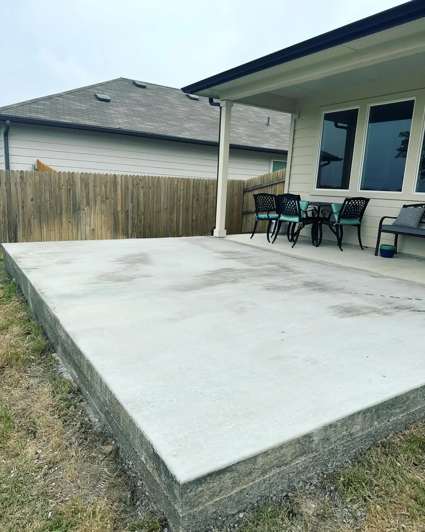 Empty concrete backyard patio with outdoor furniture and a wooden fence.