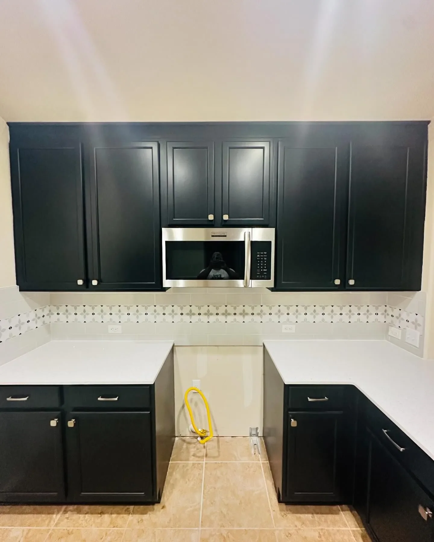 Kitchen with black cabinets, white countertops, a stainless steel microwave, and beige tiled floor.