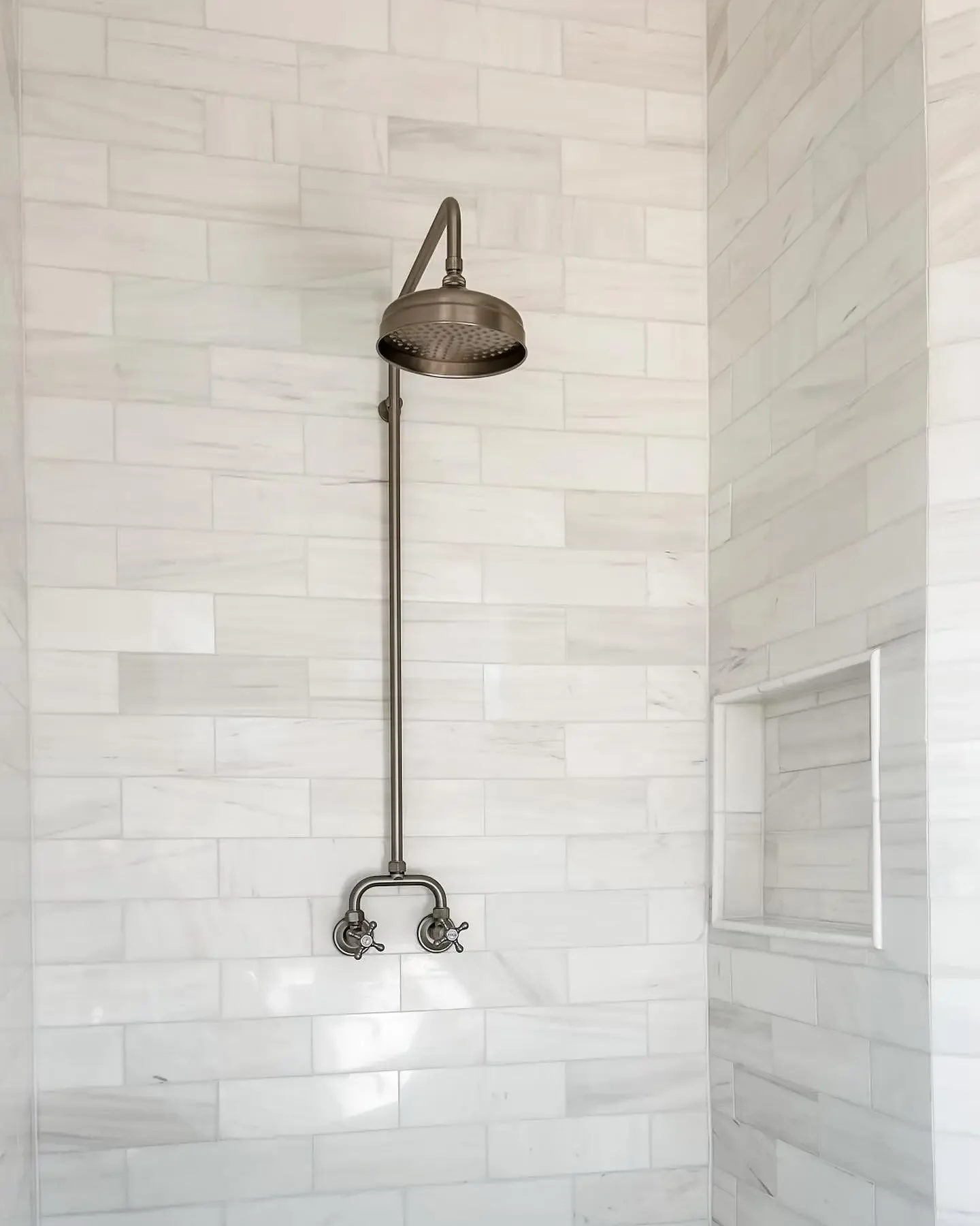 A walk-in shower with a stainless steel showerhead and fixtures, tiled with white marble tiles, and a built-in niche for toiletries.