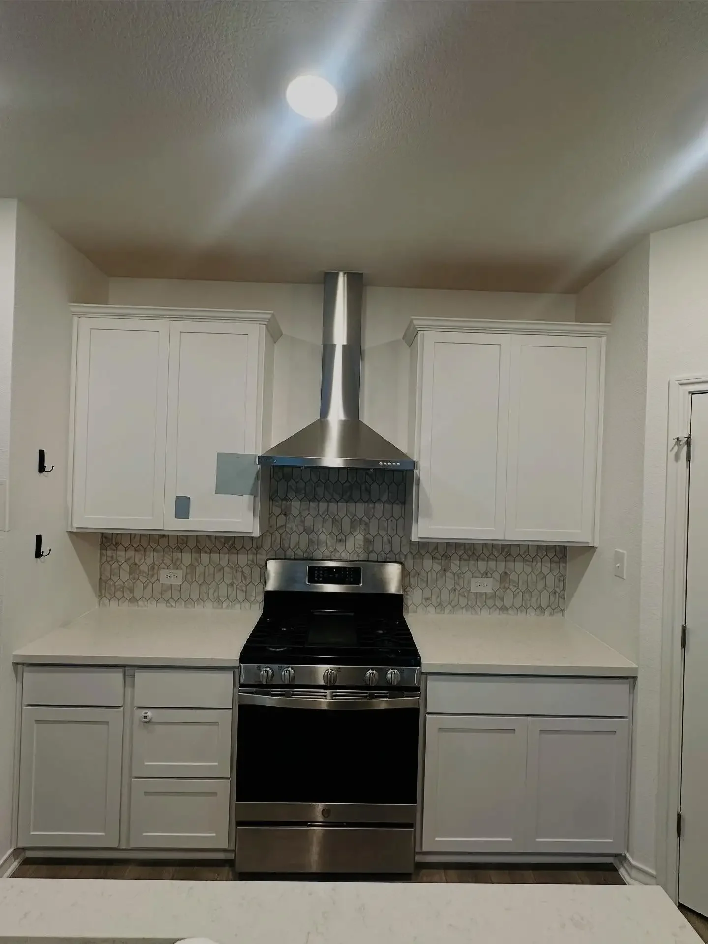 Kitchen with white cabinets, stainless steel oven and range, patterned backsplash, and white countertops.