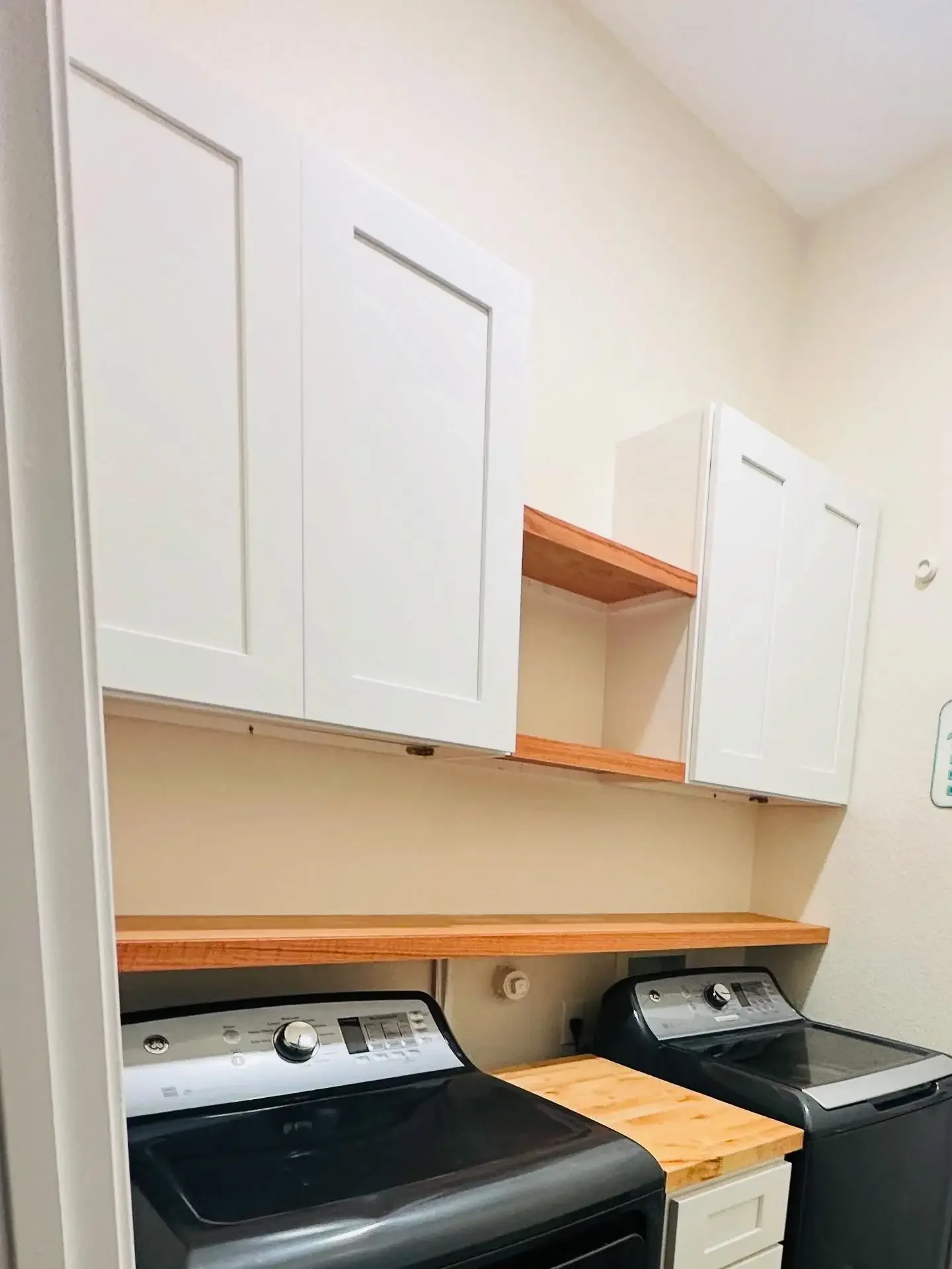 Laundry room with white cabinets, a wooden countertop, and a black top-loading washing machine and dryer.