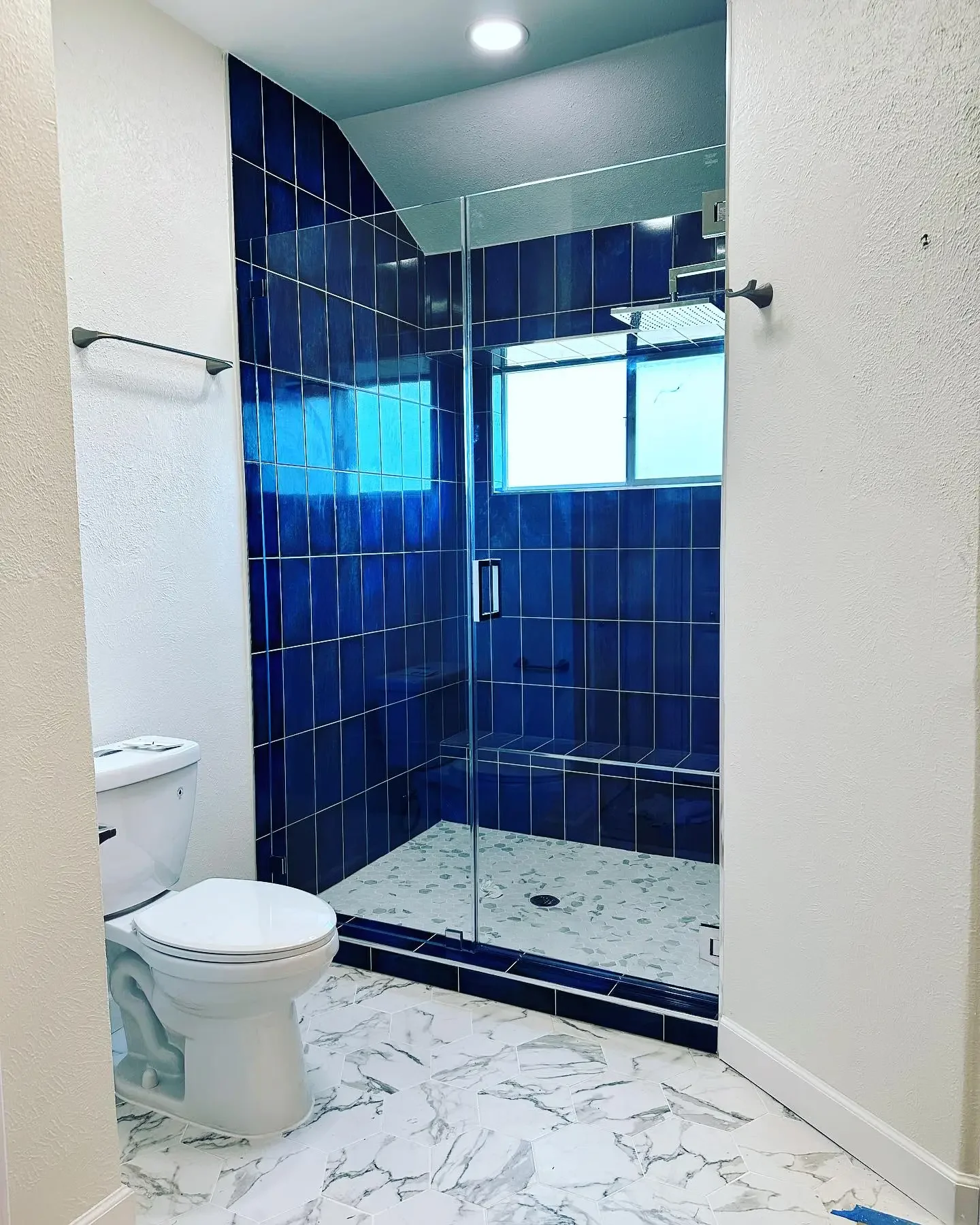 Bathroom with white marble floor, white toilet, and a glass-enclosed walk-in shower with blue tiles and a small window.
