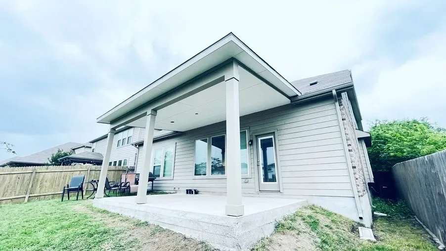 The photo shows the back of a modern house with a covered patio, outdoor seating, and a fenced backyard with grass.