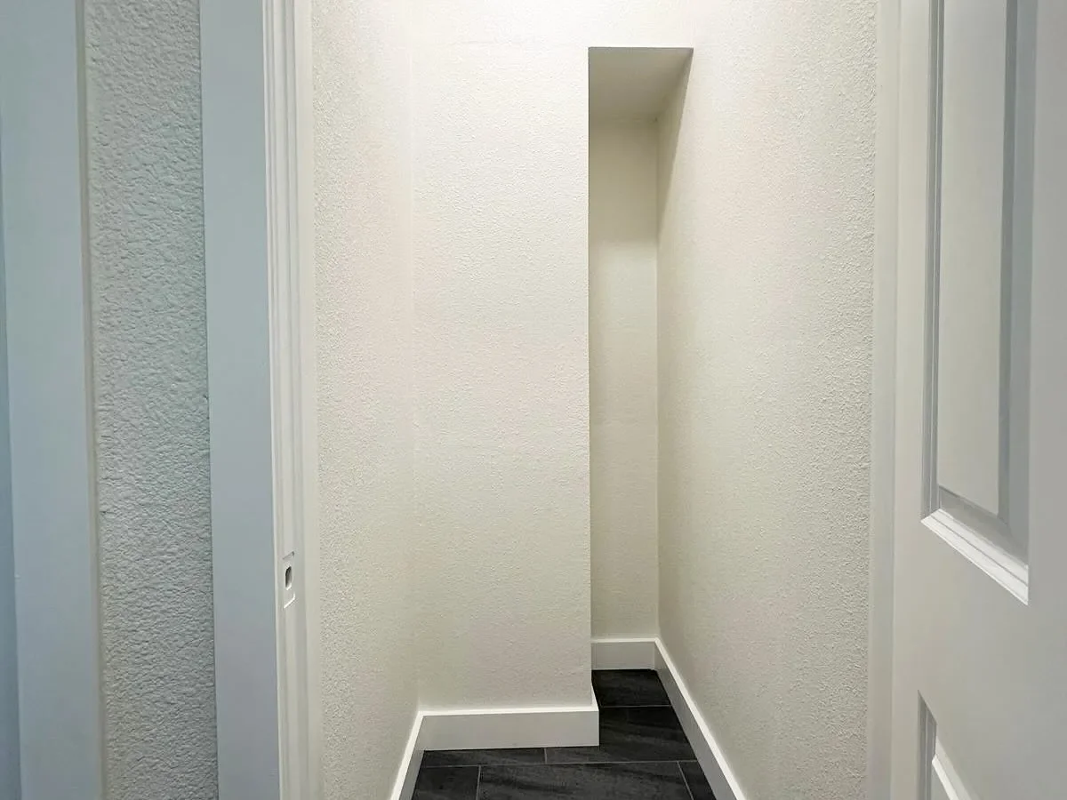 Empty narrow hallway or alcove with textured white walls and dark flooring.