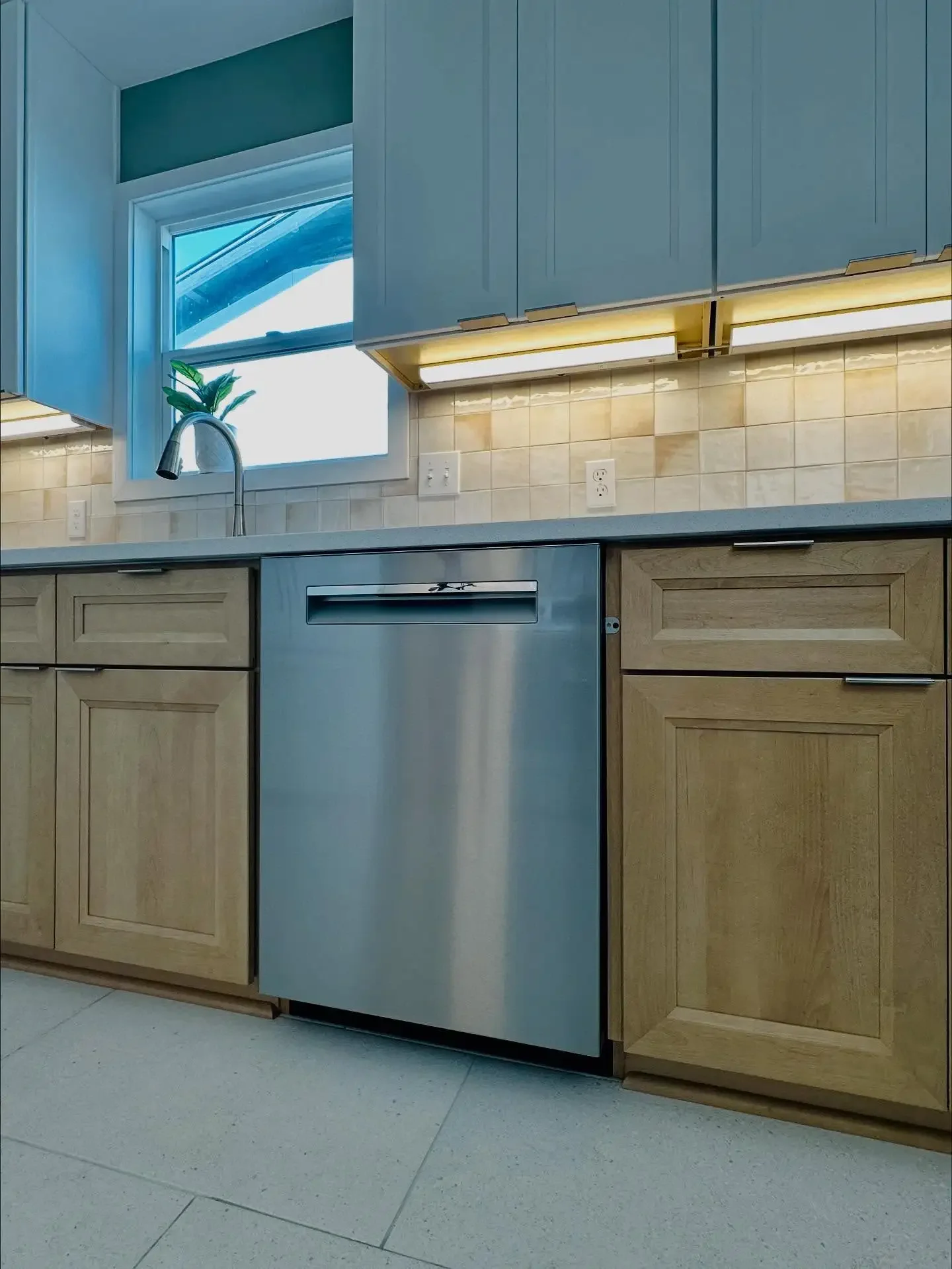 Kitchen with wooden cabinets, a stainless steel dishwasher, a window above the sink, and a backsplash with beige tiles.